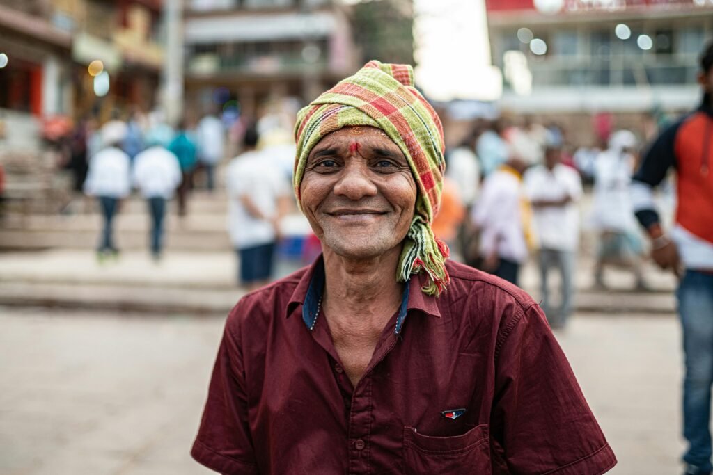 A joyful man in traditional attire smiles warmly in a bustling Varanasi street.